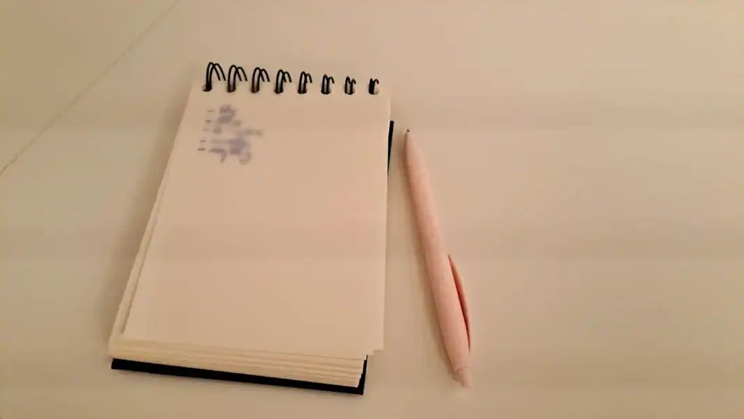 Carnet cu o listă scrisă de mână și un pix pus alături, pe o masă goală